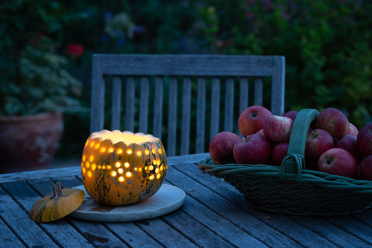 Leuchtender Halloweenkürbis und ein Korb roter Äpfel zur blauen Stunde